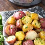 Potatoes with Herb Butter in a white bowl in front of a pressure cooker