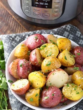 Potatoes with Herb Butter in a white bowl in front of a pressure cooker