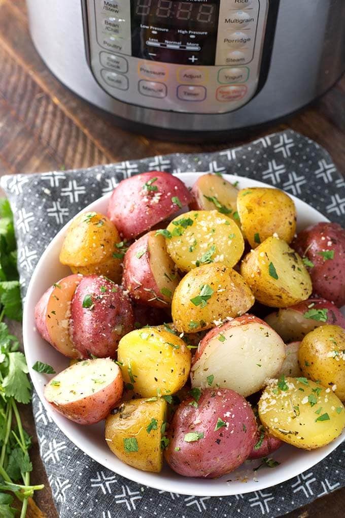 Potatoes with Herb Butter in a white bowl on top a black and white patterned napkin all in front of a pressure cooker