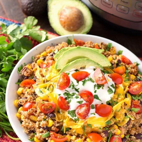 Quinoa Taco Bowl in a white bowl next to a fresh bunch of cilantro all in front of a pressure cooker
