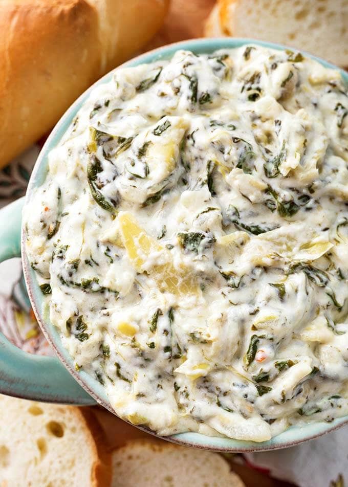 Close up of Spinach Artichoke Dip in a turquoise bowl next to slices of bread