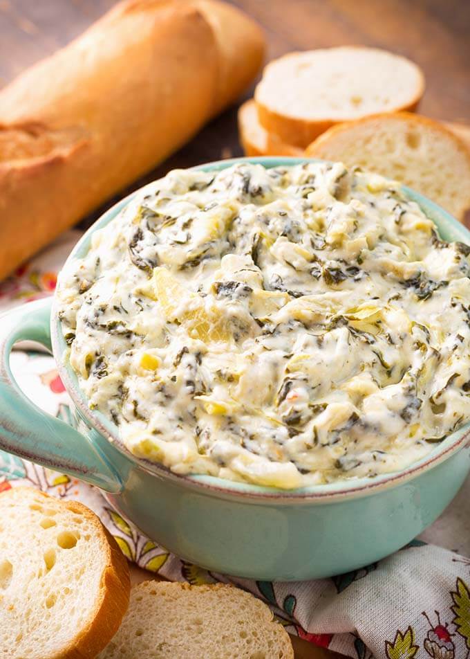 Spinach Artichoke Dip in small turquoise bowl with handles next to slices of bread