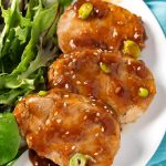 Sliced Teriyaki Pork Tenderloin with leafy green vegetables on white plate