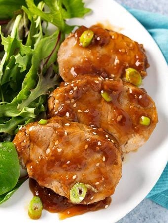 Sliced Teriyaki Pork Tenderloin with leafy green vegetables on white plate