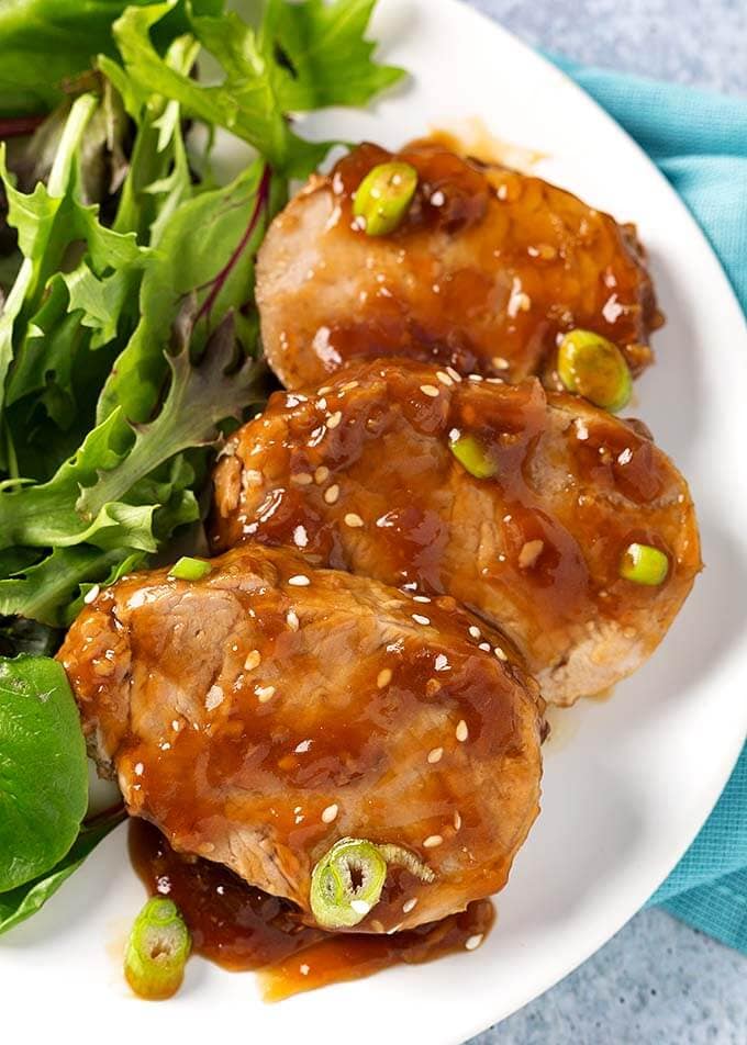 Slices of Teriyaki Pork Tenderloin with green leafy vegetables on white plate