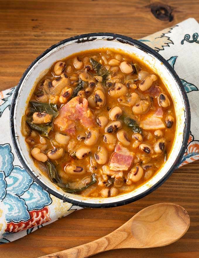 Black Eyed Peas in a white bowl with black rim on a floral napkin next to a wooden spoon