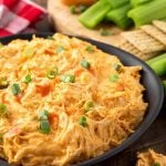 Buffalo Chicken Dip in a black bowl in front of a wooden board with crackers and celery