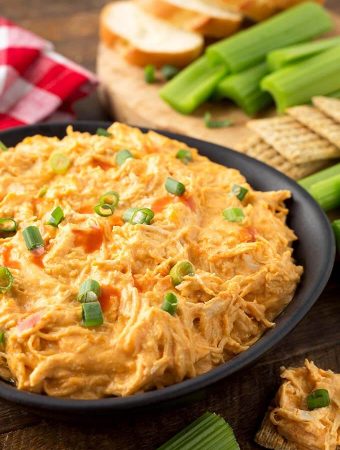 Buffalo Chicken Dip in a black bowl in front of a wooden board with crackers and celery