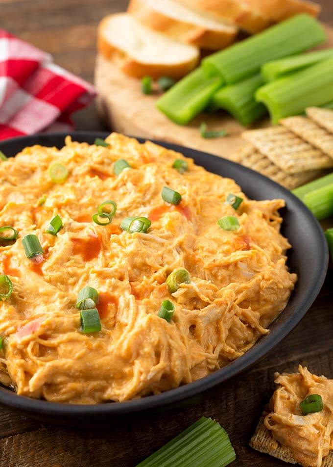 Buffalo Chicken Dip in a black bowl in front of a wooden board with crackers and celery