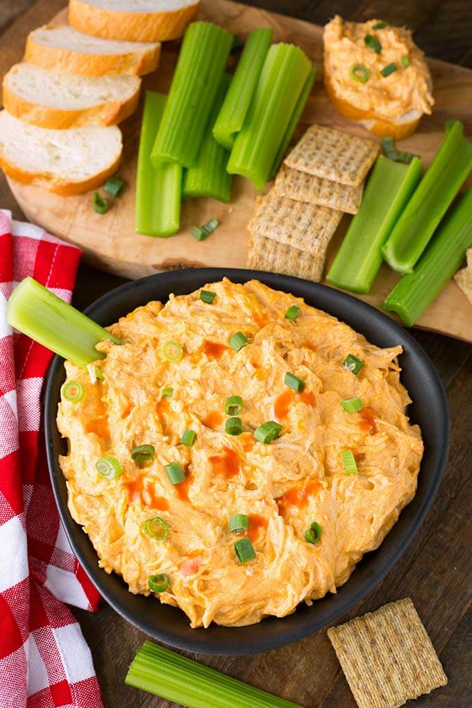 Top view of Buffalo Chicken Dip in a black bowl and a wooden board with cilantro, crackers, and sliced bread