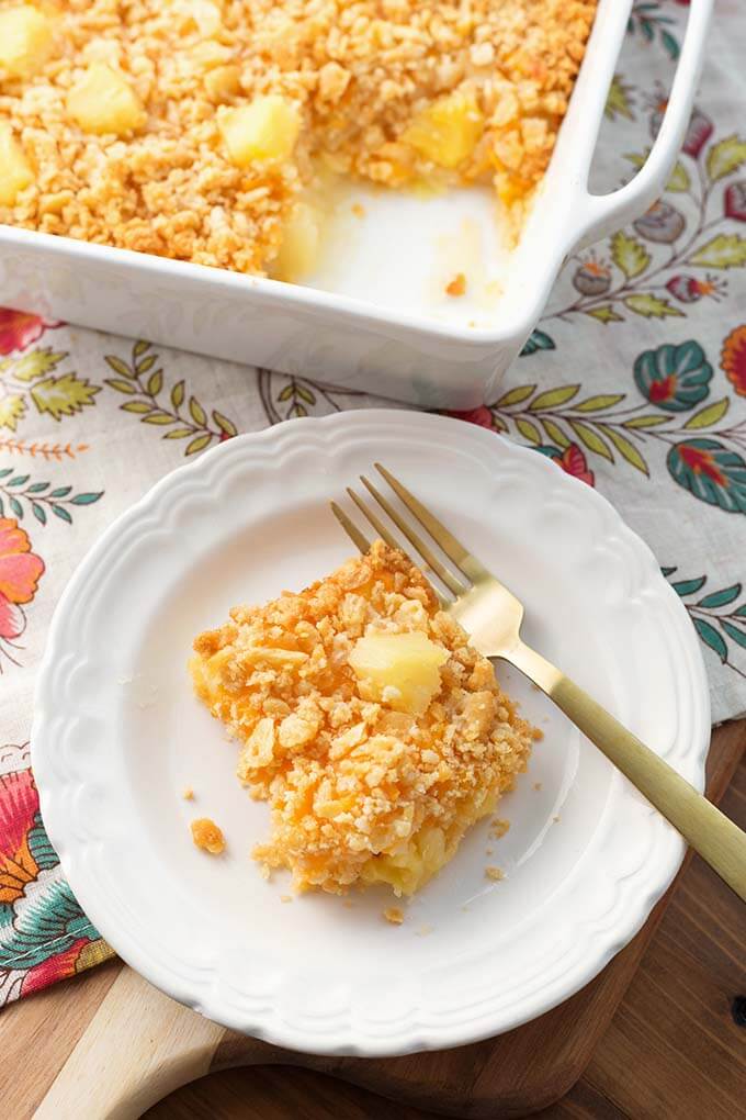 Slice of Pineapple Casserole on a white plate with golden fork in front of white baking dish
