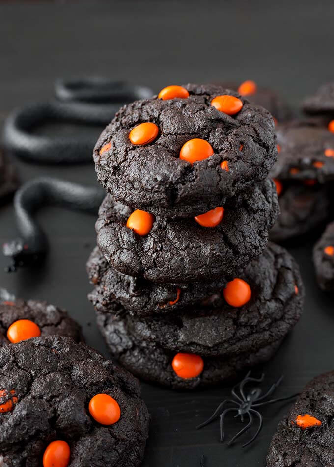 Closeup of Four Dark Chocolate Halloween Cookies stacked next to black plastic spiders and snakes