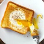 egg in a hole serving on white plate with forkful taken out and yolk runny