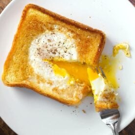 egg in a hole serving on white plate with forkful taken out and yolk runny