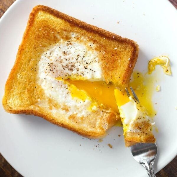 egg in a hole serving on white plate with forkful taken out and yolk runny