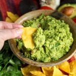 Hand dipping corn tortilla chip into Fresh Homemade Guacamole