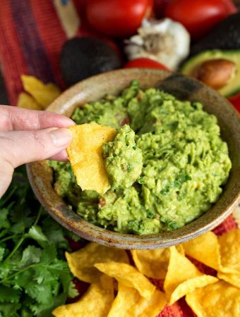 Hand dipping corn tortilla chip into Fresh Homemade Guacamole