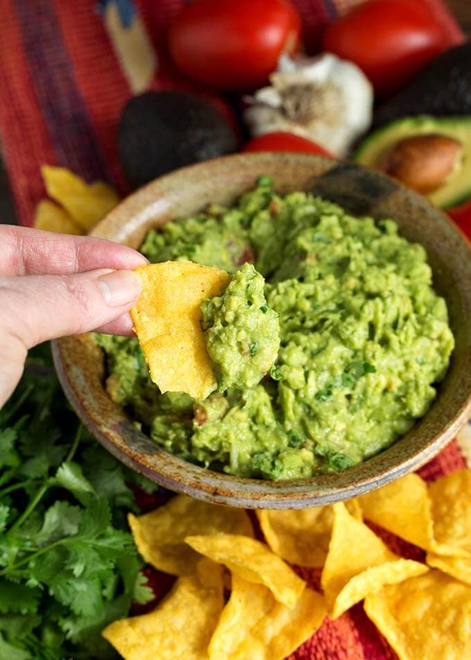 Hand dipping corn tortilla chip into brown bowl of Fresh Homemade Guacamole