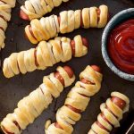 Halloween Hot Dog Mummies on baking sheet with small bowl of ketchup