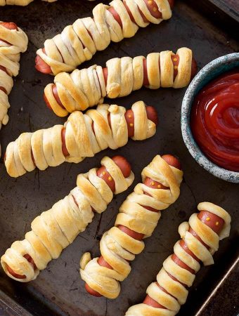 Halloween Hot Dog Mummies on baking sheet with small bowl of ketchup