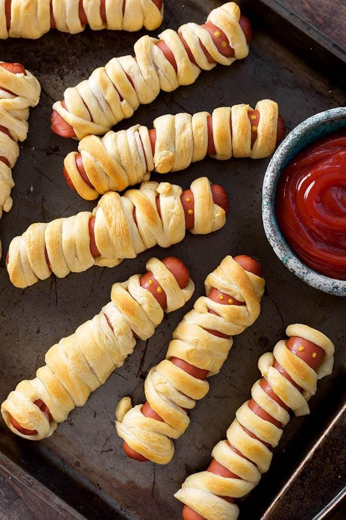 Halloween Hot Dog Mummies on baking sheet with small bowl of ketchup