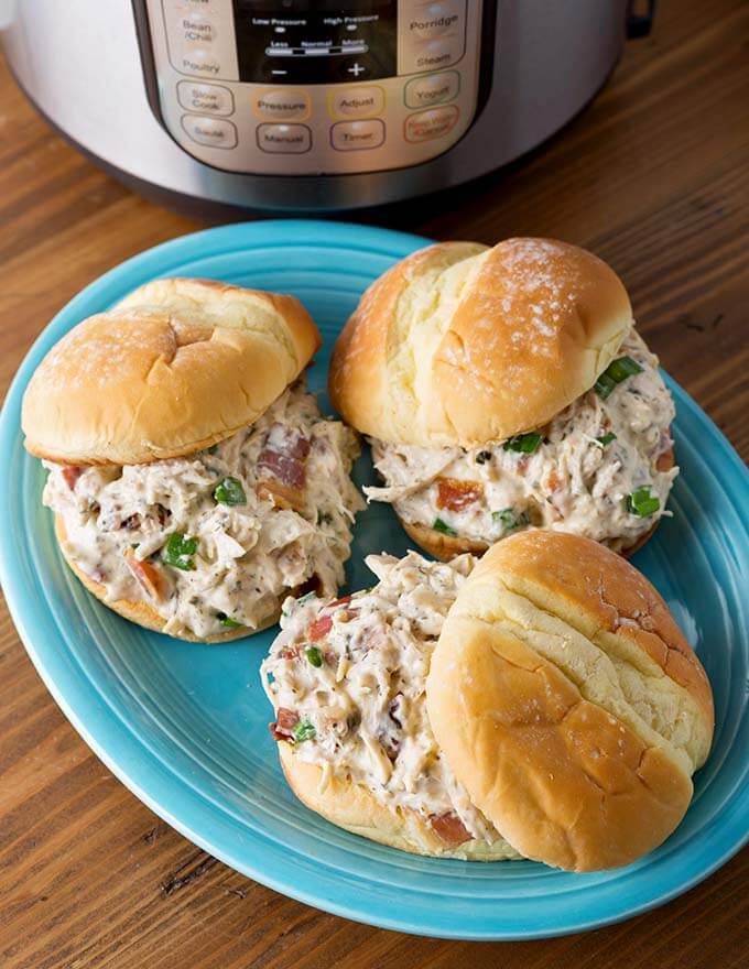 Three hamburger buns with Crack Chicken on blue plate in front of a pressure cooker