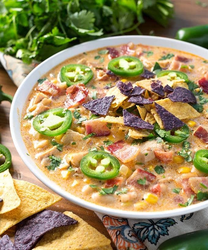Jalapeño Popper Chicken Chili in a white bowl next to herbs and tortilla chips
