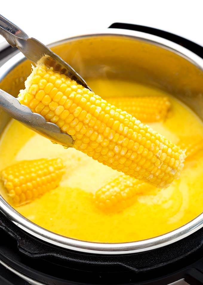 Tongs taking out ear of Milk and Honey Corn on the Cob from pressure cooker