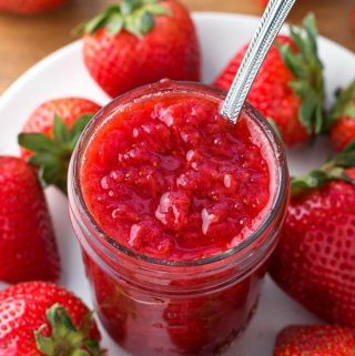 Strawberry Jam in small canning jar on white plate surrounded by strawberries