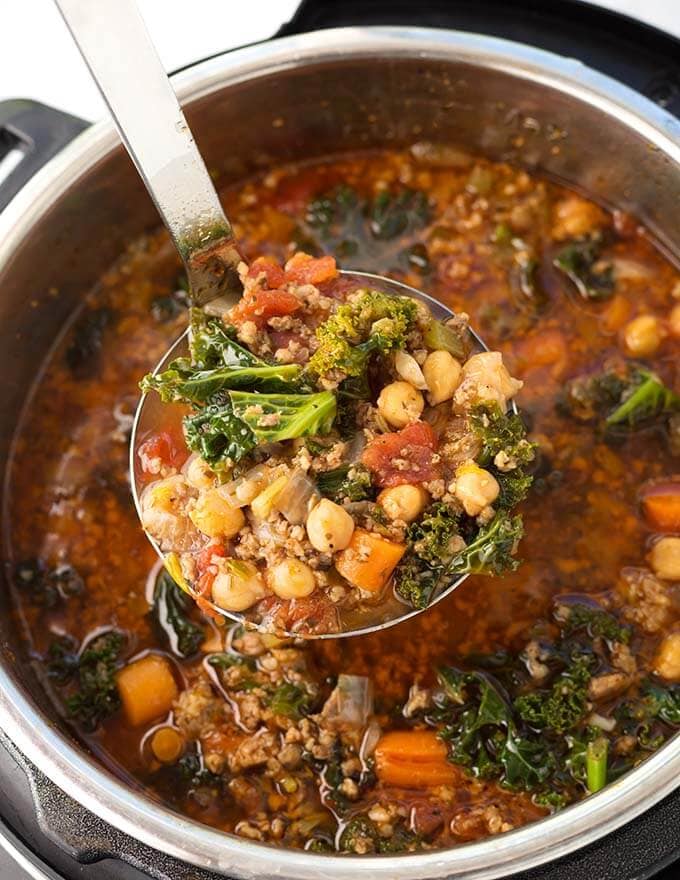 Closeup of ladle full of Tuscan Sausage Kale Soup over pressure cooker