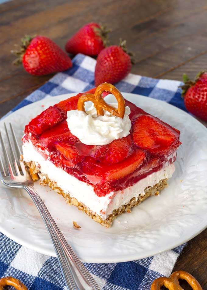 Slice of Strawberry Pretzel Jello Salad on white plate with silver fork on blue gingham napkin