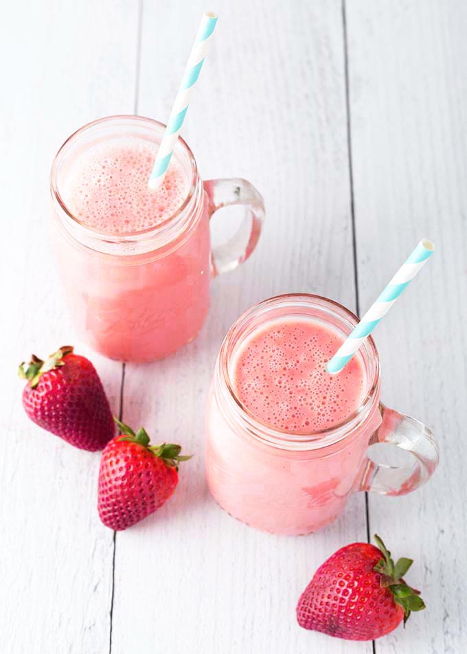 Two Sunshine Smoothies in glass mugs with stripped straws on light wood background