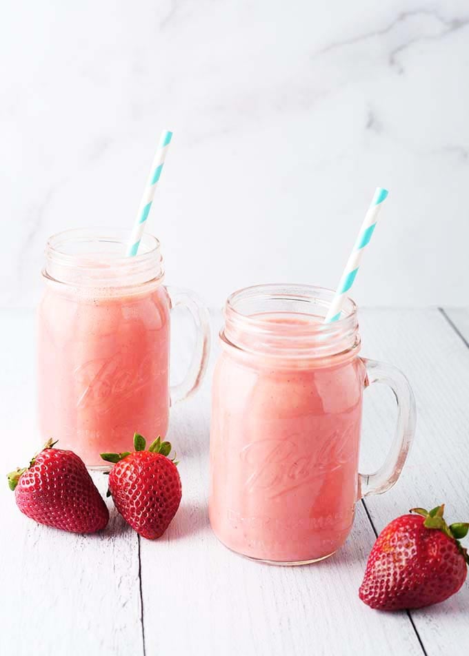 Two Strawberry Sunshine Smoothies with stripped straws in glass mugs next to strawberries