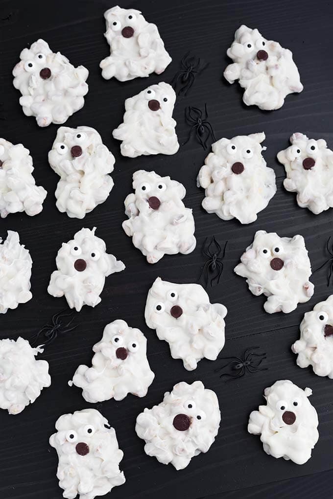 Several White Chocolate Halloween Ghosts and black plastic spiders on dark wood background