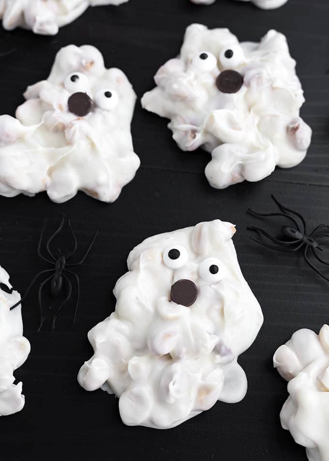 Closeup of White Chocolate Halloween Ghosts on a dark wood background with black plastic spiders