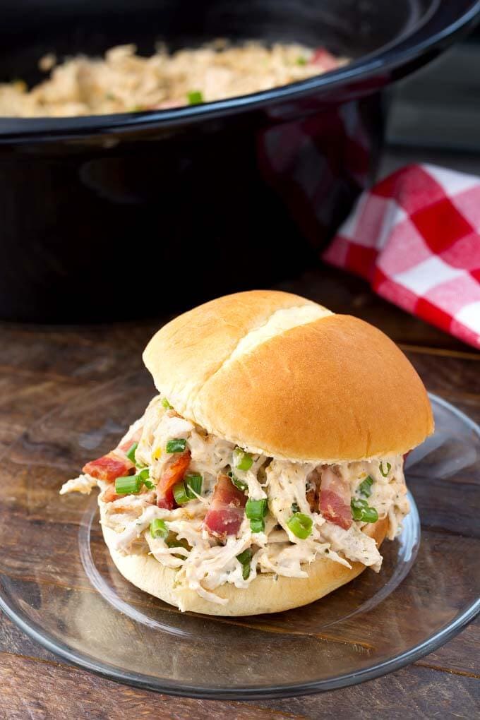 Crack Chicken on a hamburger bun on a glass plate in front of a slow cooker