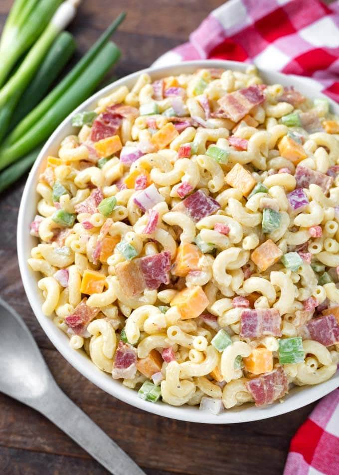 Classic Macaroni Salad in a white bowl on wooden background next to silver spoon