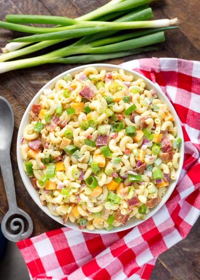 Top view of Classic Macaroni Salad in white bowl next to red gingham napkin and silver spoon