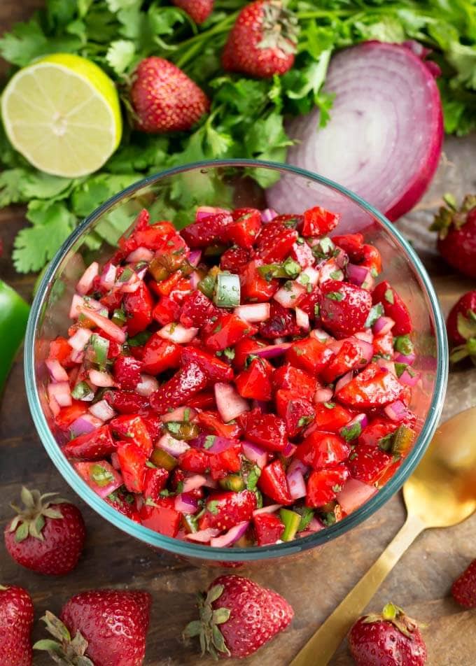 Fresh Strawberry Salsa in glass bowl next to herbs, fruit, and vegetables