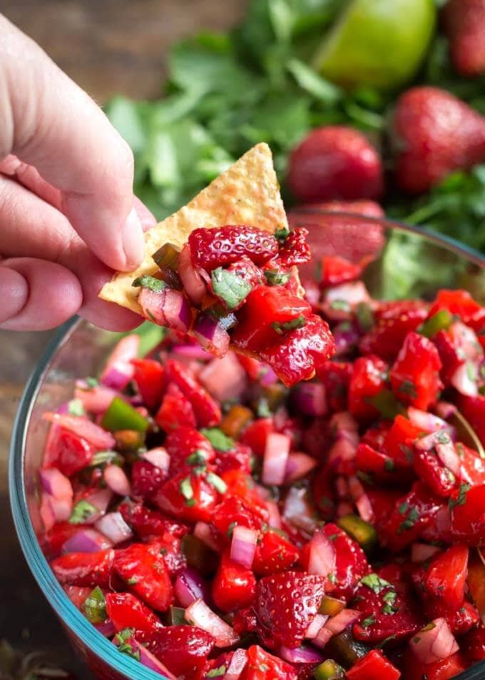 hand using tortilla chip to scoop up Fresh Strawberry Salsa in glass bowl