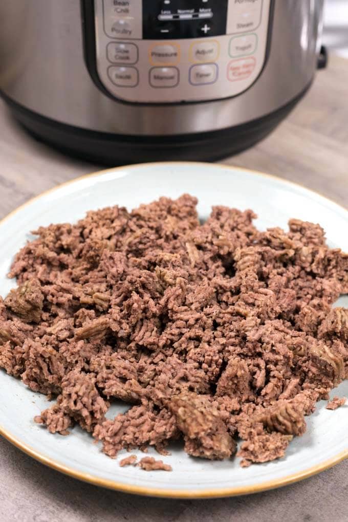 Cooked Ground Beef on gray plate in front of pressure cooker