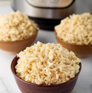 Three brown bowls of brown rice in front of pressure cooker