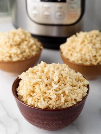 Three brown bowls of brown rice in front of pressure cooker