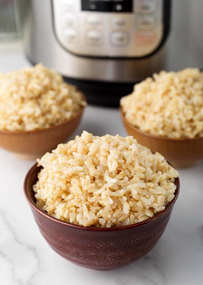 Three brown bowls of brown rice in front of pressure cooker