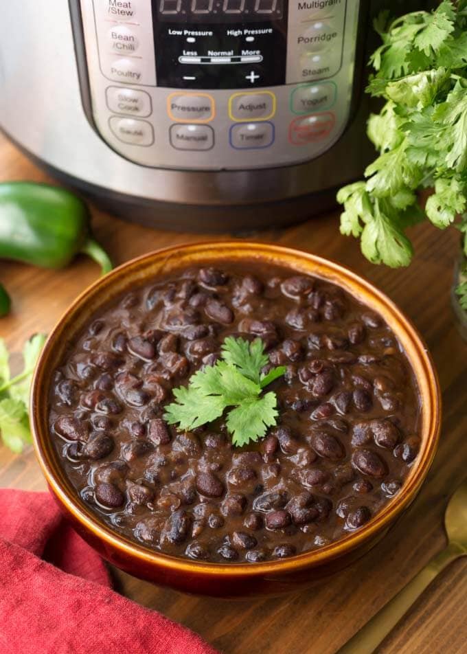 Cuban Black Beans in a brown bowl in front of pressure cooker