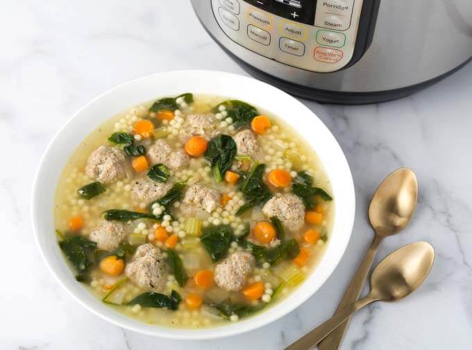 Italian Wedding Soup in white bowl next to two spoons in front of pressure cooker