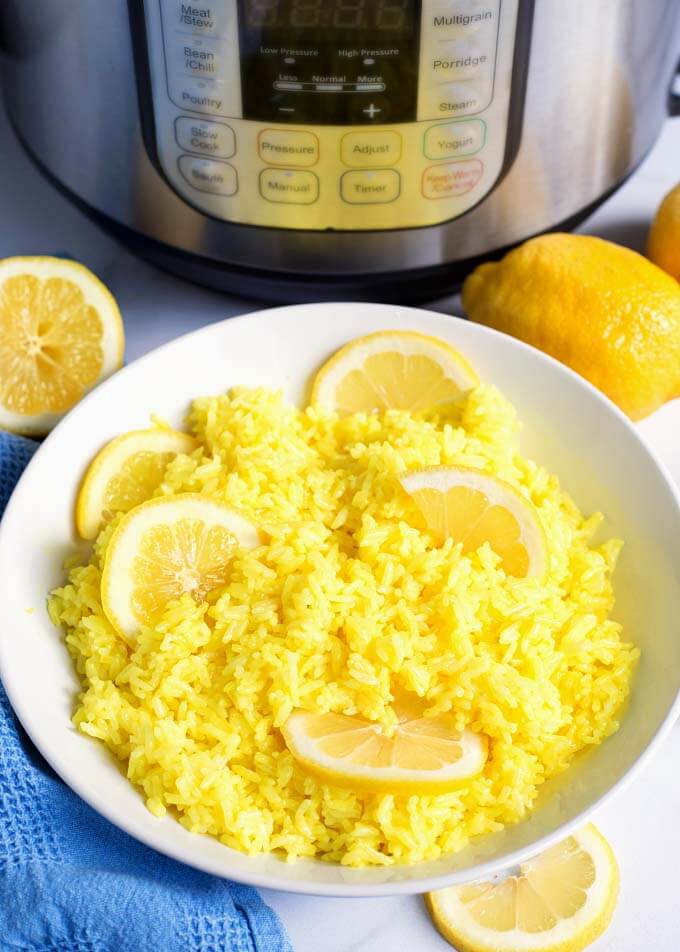 Lemon Rice in a white bowl with sliced lemons in front of pressure cooker