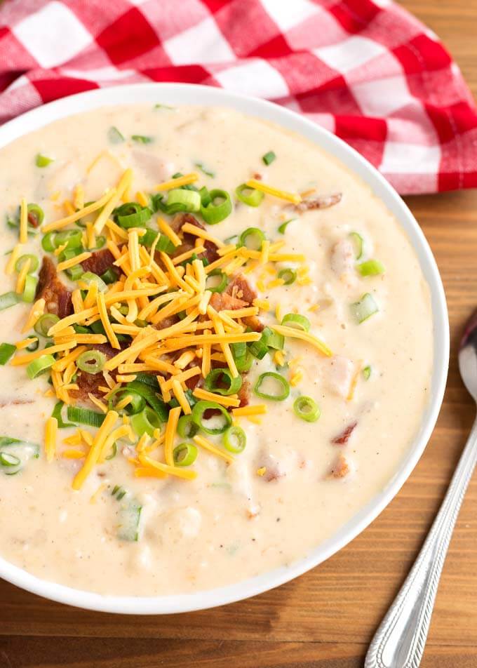 Loaded Potato Soup in a white bowl next to spoon on wooden surface