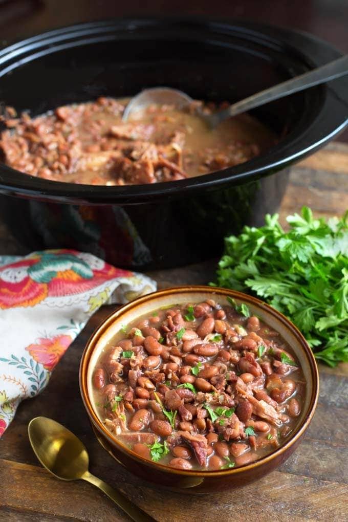 Pinto Beans and Ham in bowl with brown rim in front of slow cooker