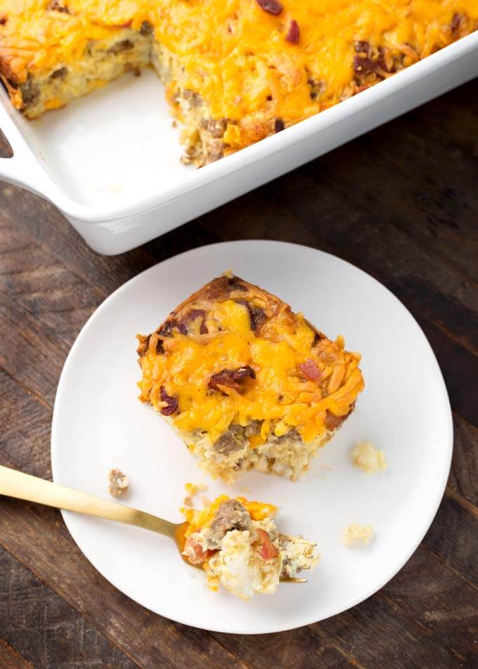 Slice of Tater Tot Breakfast Casserole on a white plate in front of the white baking dish of the rest of the casserole